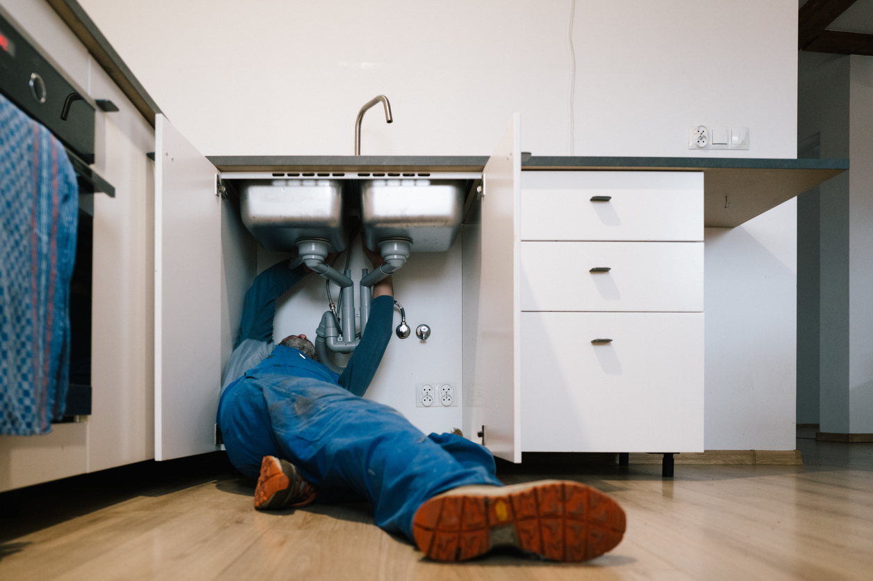 Plumber working beneath a sink providing plumbing services in Nashville.