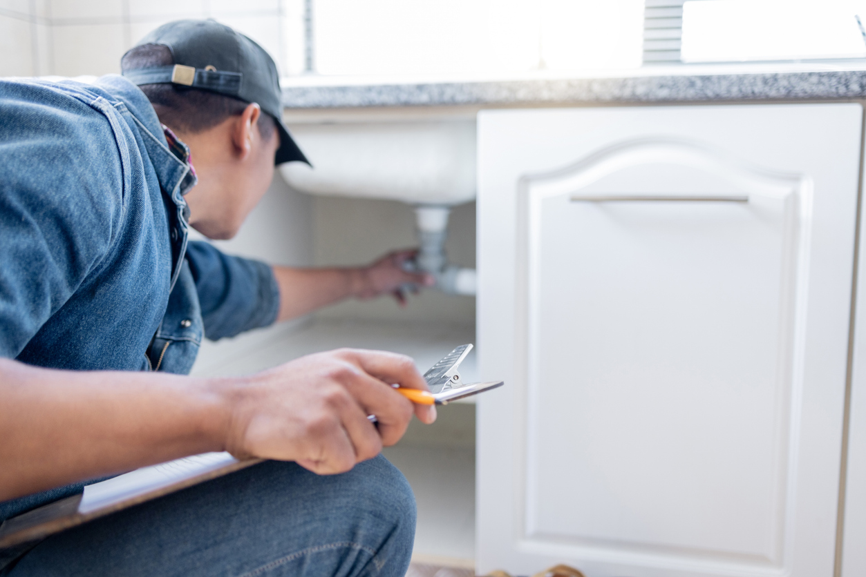 Plumber repairing plumbing fixtures beneath a bathroom sink.