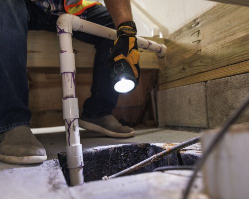 Technician inspecting a residential sump pump system in a basement.