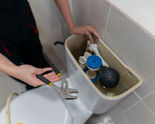 Plumber repairing toilet components in a residential bathroom.